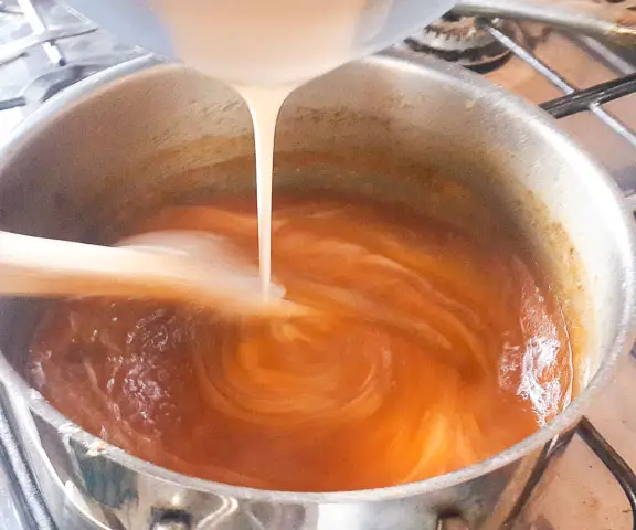pouring corn paste into pot of agidi jollof