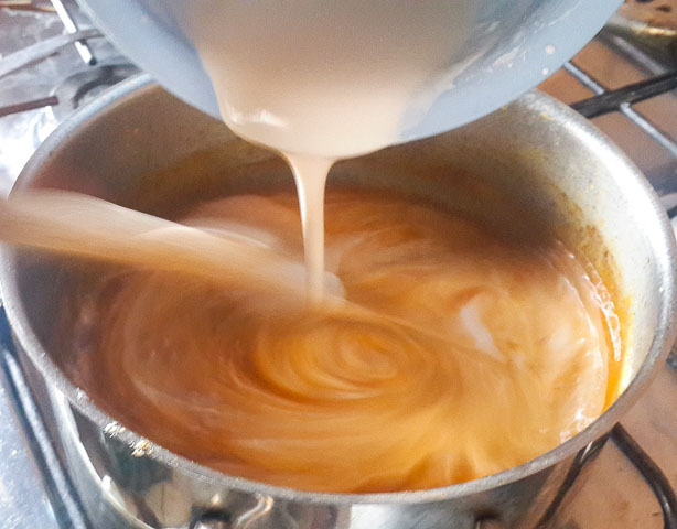 pouring corn paste into pot of agidi jollof