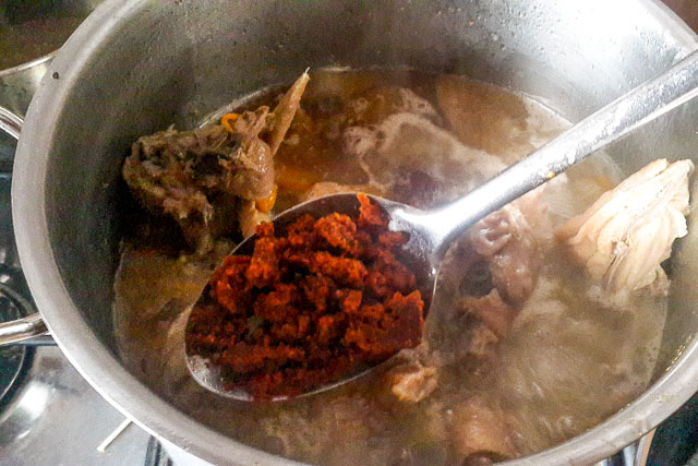 tomato paste roux being scooped into the meat stock for tomato paste and roux for quick and easy tomato sauce