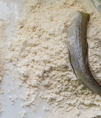 white bait being dipped in seasoned flour for Nigerian crispy fried whitebait fish