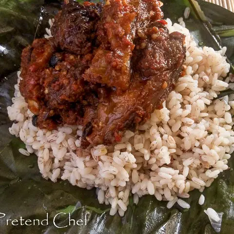 Hot and spicy ofada rice and stew served in fresh banana leaves